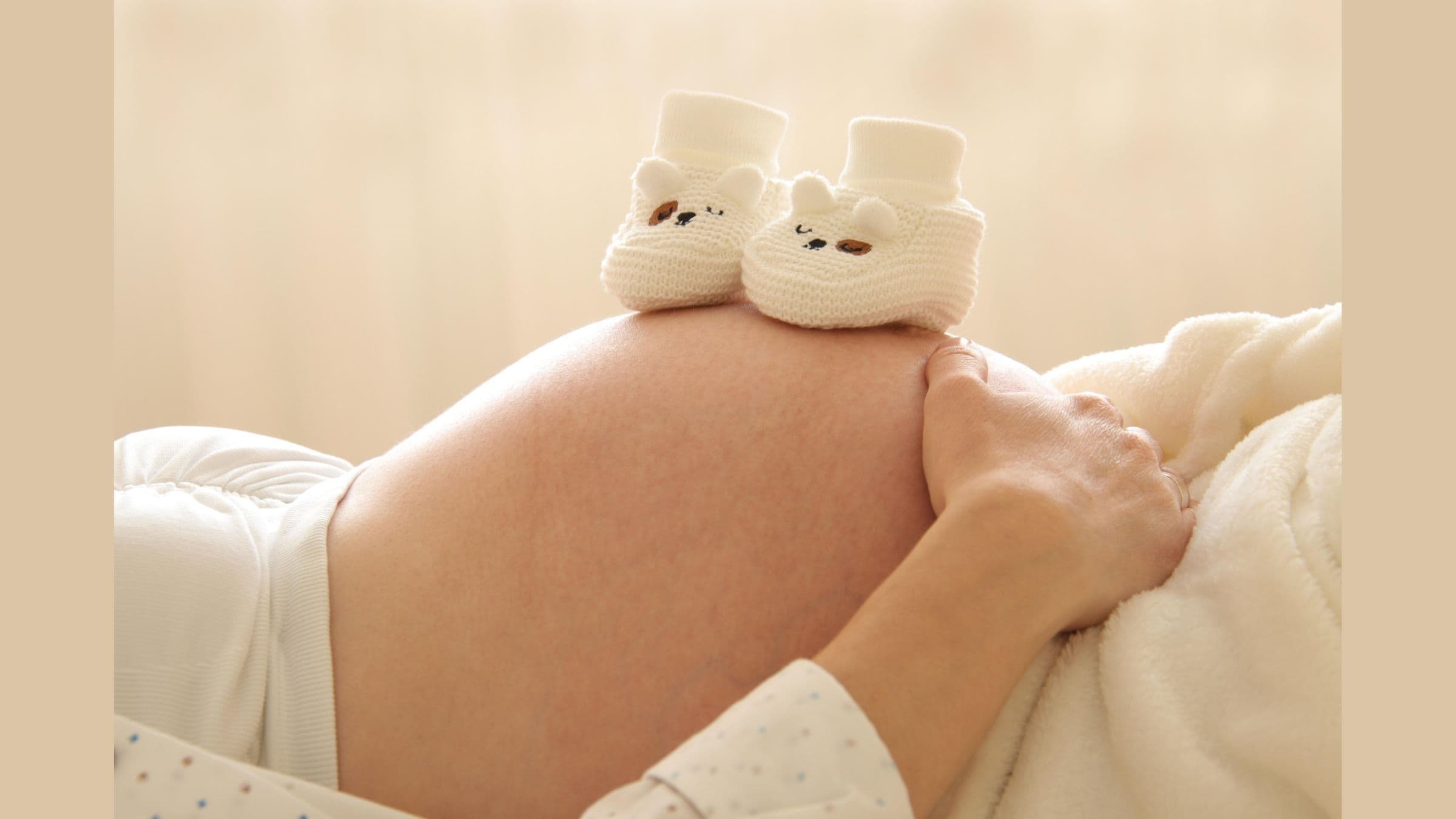 Donna in gravidanza con scarpine da neonato sul pancione, simbolo dell'attesa della nascita.